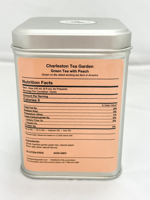 Rectangular metal tea tin labeled Charleston Tea Garden Green Tea with Peach, featuring a peach colored label with nutrition facts and ingredient details