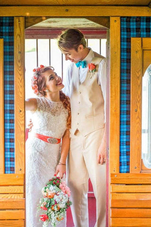Bride and groom smiling at each other while standing in a wooden doorway, with the bride holding a colorful bouquet and wearing a floral crown.