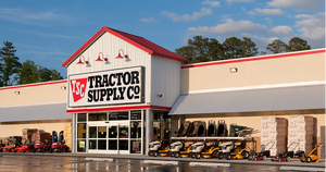 Tractor Supply Co. storefront with red and white signage, outdoor equipment displayed along the entrance, and a partly cloudy blue sky overhead.