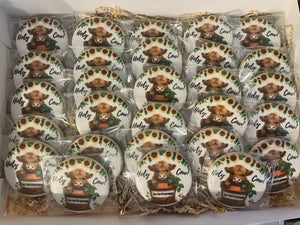 Rows of round cow themed souvenirs wrapped in clear plastic, featuring Highland cattle, sunflower accents, and the phrase Holy Cow.