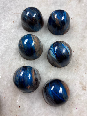 Six polished dark blue and black rounded stones with brown streaks arranged on a light marble surface.