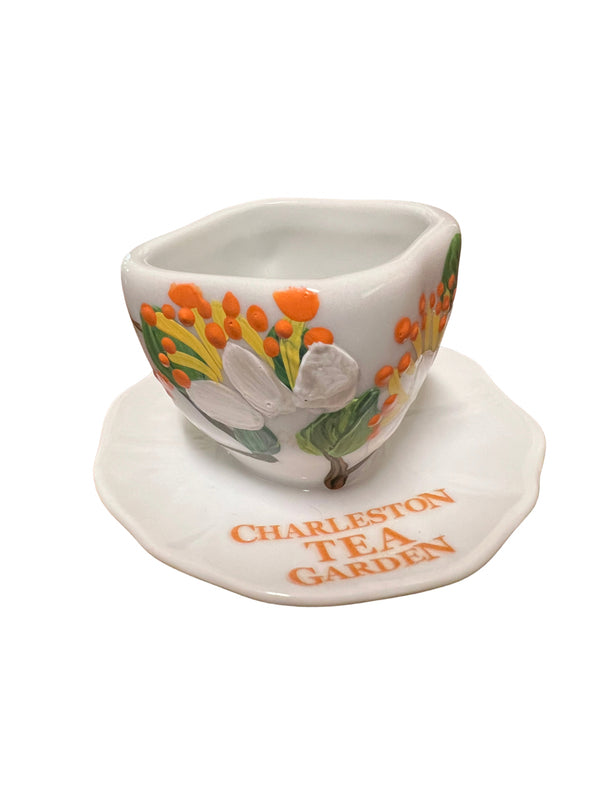 Decorative ceramic tea cup ornament with a floral orange and white design, displayed on a matching saucer marked Charleston Tea Garden