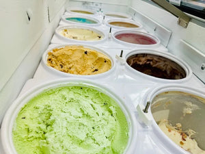 Close-up view of a variety of ice cream flavors in a freezer, including green, chocolate, and fruit-flavored options, arranged in round containers.