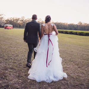 Newlywed couple walking hand in hand across a grassy field, with the bride in a flowing white gown and the groom in a dark suit at Charleston Tea Garden