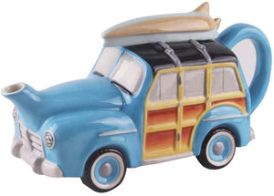 Ceramic teapot shaped like a vintage woody station wagon with blue body and wooden panel details, featuring a surfboard on the roof and a curved handle.